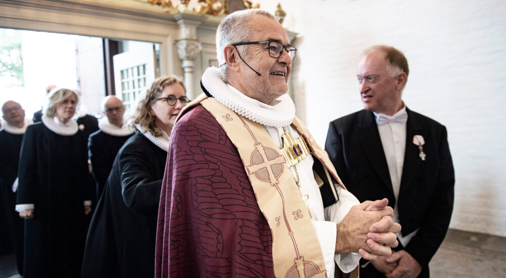 Biskop med stort smil og knyttede hænder træder ind i kirken